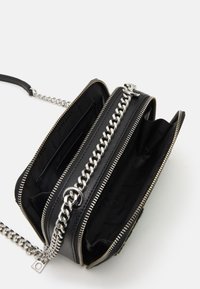 Borsa in finta pelle nera con tracolla in catena argentata, chiusura a zip e più scomparti. L'interno è foderato in nero con stampa del logo.