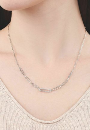 Silver chain necklace with elongated oval links and one central link adorned with small sparkling crystals on a person wearing a beige top.