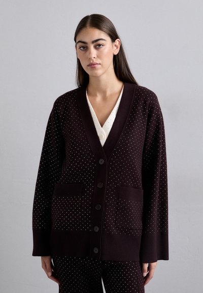 Dunkelburgunderfarbener Cardigan mit weißen Punkten. Mit V-Ausschnitt, langen Ärmeln, großen vorderen Taschen und schwarzen Knöpfen. Strickstruktur.