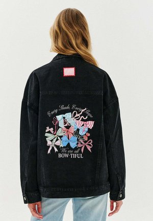 Černá džínová bunda s barevným grafickým motivem různých mašlí na zádech, s textem "Všichni jsme BOW-TIFUL." Červená čtvercová nášivka.