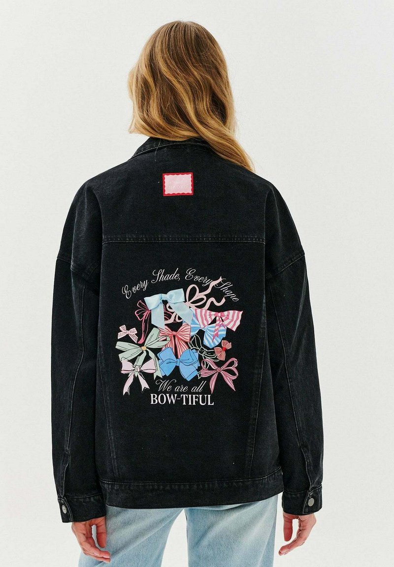 Czarna kurtka dżinsowa z kolorową grafiką różnych kokard na plecach, z napisem "Wszyscy jesteśmy BOW-TIFUL". Czerwona naszywka w kształcie kwadratu.