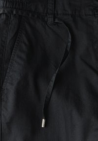 Svarta vävda shorts med platt framsida, elastisk midja och dragsko med metallspets. Slät textur och avslappnad design.