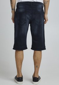 Shorts en denim foncé à coupe droite, avec un ourlet roulé, un design à cinq poches et une légère décoloration. Portés avec des baskets noires.