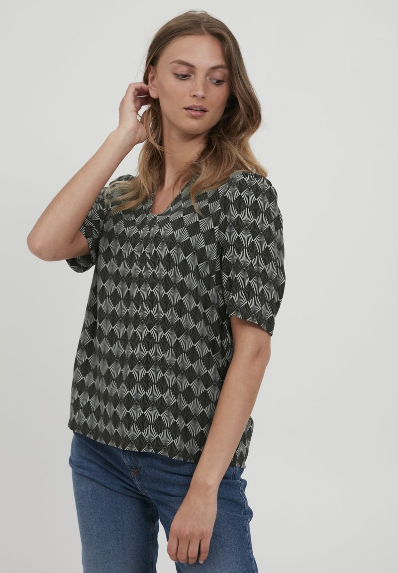 Maglietta a maniche corte bianca e nera con scollo a V, caratterizzata da un design geometrico e una vestibilità comoda, abbinata a jeans in denim blu.