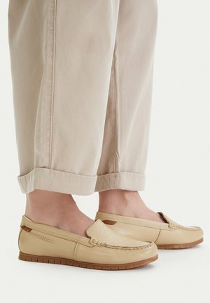 Mocassini beige in pelle senza lacci indossati con pantaloni beige chiaro con risvolto, mostrati di lato e dall'alto su sfondo bianco.