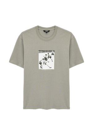 Jasnoszary T-shirt z krótkim rękawem z czarno-białą sceną hokeja na lodzie na przodzie oraz napisem "Bądź czujny, graj ostro."