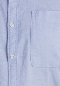 Camicia azzurro chiaro con bottoni, realizzata in tessuto intrecciato, dotata di taschino sul petto con bordo arrotondato e bottoni in plastica bianca.