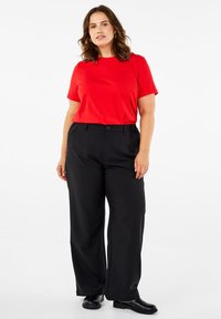 Raudonas trumpomis rankovėmis marškinėlis derinamas su juodomis plačiomis kelnėmis. Apranga pasižymi paprastu dizainu ir pagaminta iš lygaus, lengvo audinio.