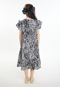 Vestito a pois bianco e nero con maniche a sbuffo e orlo arricciato, abbinato a scarpe dorate senza tacco. Capelli legati con un grande fiocco nero.