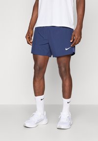 Granatowe spodenki sportowe z elastycznym pasem, z białym logo Nike z boku. Noszone z białymi skarpetkami i butami.