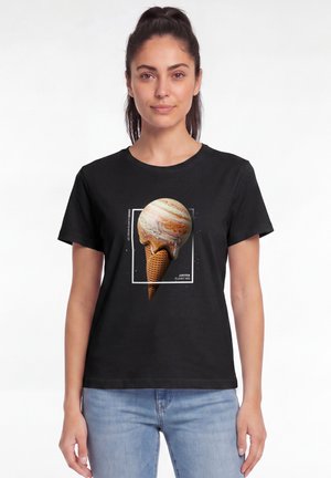 Frau trägt ein schwarzes T-Shirt mit einem schmelzenden Jupiter-Planet, der als Eistüte gestaltet ist, und hellblaue Jeans.