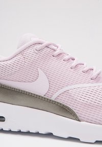 Zapatillas de deporte de color rosa claro con un upper de malla texturizada, acentos blancos y una entresuela gris. Presenta un diseño con cordones y una marca prominente.