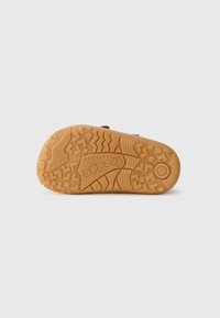 Semelle de chaussure en caoutchouc avec un motif texturé pour une meilleure adhérence. Comprend un logo circulaire et un profond relief pour la traction. La couleur est beige.
