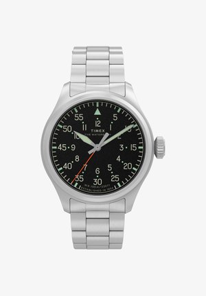 Ura Timex Waterbury z jeklenim jermenom, črnim številčnico, svetlečimi kazalci in rdečo sekundno ročico, ki kaže čas 10:08:35.