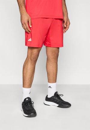 Rote sportliche Shorts mit schlichter Optik und einem weißen Adidas-Logo auf der linken Seite. Kombiniert mit schwarzen Schuhen und weißen Socken.