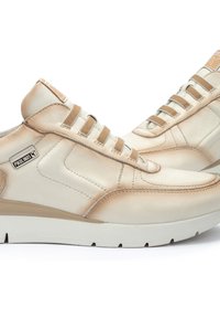 Baskets en cuir beige avec une texture lisse, dotées d'une semelle blanche, de six œillets et d'un patch logo sur le côté.