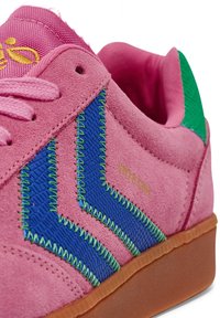 Rosa mockakängor med blå och gröna zickzack-sömmar, gröna accenter och en beige gummisula. Guldlogotyp finns på sidan.