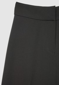 Pantaloni neri con finitura in tessuto liscio, caratterizzati da una cintura larga e una tasca laterale discreta sul lato sinistro, design minimalista.