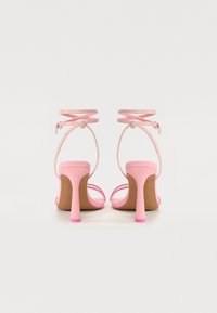 Sandali con tacco rosa con fettucce sottili e design incrociato sulla caviglia. Il tacco è alto e leggermente svasato, con una base rosa solida.