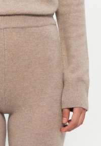 Beige gebreide trui met geribde manchetten, met een zachte textuur en aansluitende pasvorm, die tot de pols reikt, gecombineerd met bijpassende zachte broeken.