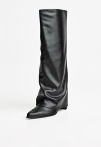 Botte noire en cuir hauteur genou avec un design décontracté, bout pointu et texture lisse. Présente des détails minimalistes et un talon bas.