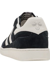 Baskets en daim noir avec des accents en cuir blanc, présentant trois rayures blanches, une semelle en caoutchouc texturé et un logo en relief sur le talon.