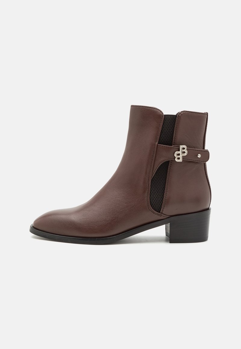 Bottine en cuir marron avec petit talon bloc, panneau élastique latéral et boucle métallique décorative sur une sangle.