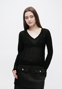 Črno dolg rokav, zgornji del z V-izrezom iz lahkega, prosojnega materiala s subtilnimi bleščicami. Združeno s črno teksturirano krilo z zlatimi gumbki kot poudarki.