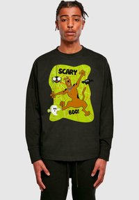 Črna majica z dolgimi rokavi, ki prikazuje risano zasnovo Scooby-Doo z napisom "SCARY BOO!", na zelenem ozadju pajčevine.