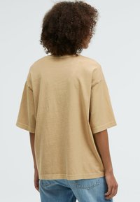 Beige oversized cotton t-shirt with short sleeves, round neckline, and a smooth texture. Styled with light blue denim jeans.