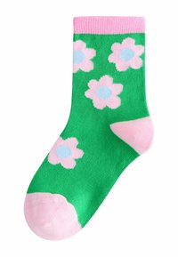 Grüne Socken mit einem gerippten rosa Bündchen, verziert mit rosa Blumen mit blauen Zentren. Das Design ist lebhaft und hat eine glatte Textur.