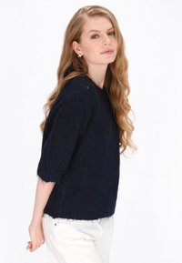 Granatowy sweter dzianinowy z rękawami o długości trzy czwarte, fakturowanym wzorem, luźnym krojem oraz frędzlami wzdłuż dolnej krawędzi.