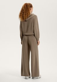 Rjav pulover s kapuco in širokimi hlačami, narejen iz mehke tkanine. Ima sproščen kroj in rebraste detajle ob šivih.