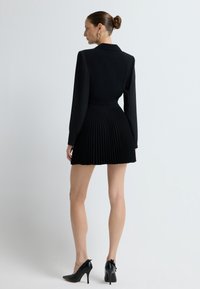 Czarna sukienka z dopasowanym, kołnierzykowym gorsetem i plisowaną spódnicą. Długie rękawy i błyszczące czarne szpilki dopełniają całość.