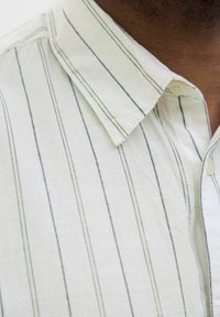 White button-up shirt featuring vertical blue stripes, a soft texture, and a classic collar. Noticeable button detail at the neck.