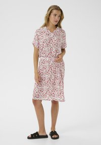 Blumenkleid mit V-Ausschnitt, kurzen Ärmeln und elastischem Bund. Es hat ein rosa-weißes Farbschema mit kleinen roten und grünen Blumen.