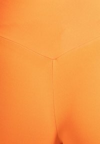 Orangefarbene Leggings mit hohem Bund aus elastischem Material, mit glatter Textur und einem markanten Nahtdetail auf der Rückseite.