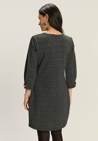 Čierno-bielé šaty so vzorom s geometrickým dizajnom, s trištvrťovými rukávmi a okrúhlym výstrihom. Strieborné gombíkmi na rukávoch.