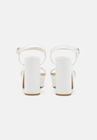 White high-heeled sandals with a chunky block heel, ankle strap, and smooth glossy finish. Features a minimal design with no patterns.
