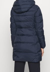 Marineblå dunjakke med hætte, med vandret quiltet design, lynlåslukning foran og elastiske manchetter. Blødt, vandafvisende materiale.