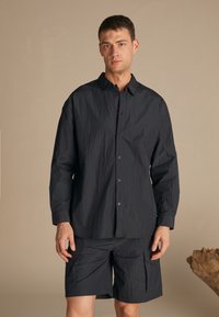Black crinkled fabric long-sleeve shirt with button closure, paired with matching cargo shorts, featuring pockets and a relaxed fit.