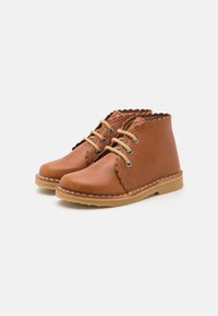 Bottines en cuir marron avec un bord festonné, bout rond et lacets beiges. Comprend un motif cousu autour de la semelle.