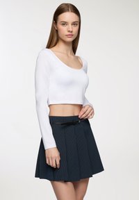 Biała długosleevowa krótka bluzka oraz granatowa spódnica w paski z czarnym akcentem w postaci paska. Gładki, jedwabisty materiał o dopasowanym kroju.