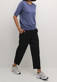 Kortærmet lavendel strikket sweater, parret med sorte bukser og grå atletiske sneakers, med en afslappet pasform og subtile teksturer.