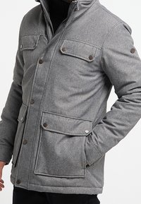 Giacca grigia realizzata in tessuto texturizzato, caratterizzata da una zip frontale, quattro tasche con chiusura a pattina e dettagli con bottoni sulle spalle.