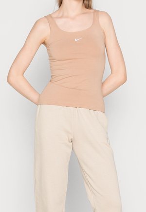 Beżowy dopasowany top na ramiączkach wykonany z elastycznej tkaniny, z okrągłym dekoltem i cienkimi ramiączkami, z małym białym logo Nike na klatce piersiowej.