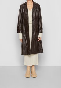 Brun läder lång kappa med snittkrage, knäppning fram och sidofickor. Bärs över en beige ribbad klänning och bruna platåstövlar.