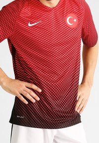 T-shirt de sport Nike Dri-FIT rouge et noir avec un motif en losange ; présente l'emblème du drapeau turc sur la poitrine et un col rond.