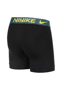 Pantalones cortos deportivos negros con una cinturilla de patrón verde y amarillo que presenta la marca "NIKE". Hechos de un material suave y elástico.