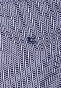 Blue fabric with a repeating small white diamond pattern and a dark emblem with text centered on the fabric.